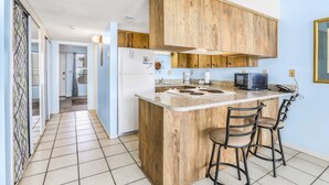 Una cocina con armarios de madera, encimera de granito y dos taburetes de bar.