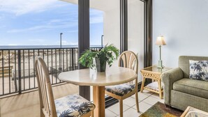 Un balcón con una mesa redonda, sillas, una planta en maceta, una lámpara y un sofá con vista a la playa.