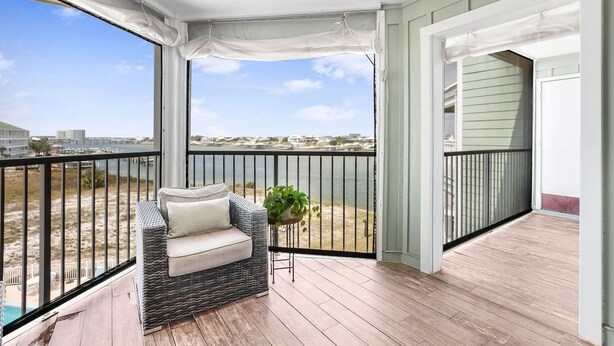 Un balcon avec un canapé en osier, une plante en pot et une vue sur la plage et le paysage urbain.