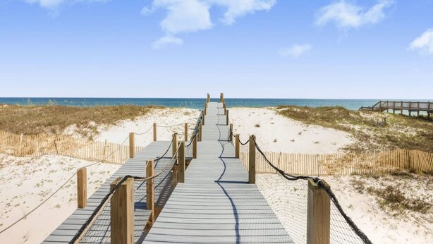A wooden boardwalk leading to a beach with a wooden fence on one side and a wooden walkway on the other. - Lagoon Time Beach Home- Elevator Beach Access (Gulf Shores)