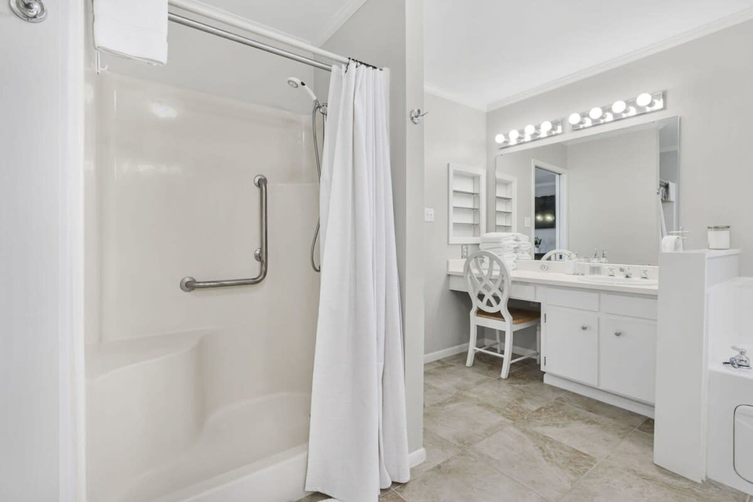 A modern bathroom with a walk-in shower, a vanity with a mirror and lights, and a chair.