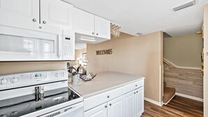 A modern kitchen with white cabinetry, a microwave, an oven, and a countertop with a 'WELCOME' sign. - Gulfside Townhome 32 Beachfront Townhouse w Pool (Gulf Shores)
