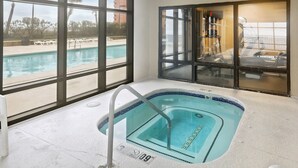An indoor swimming pool with clear views of the outside pool area, a large window, and a glass door leading to a balcony. - Grand Pointe 502- Gulf-front Water on 2 Sides (Orange Beach)