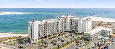 A hotel with multiple floors, a parking lot, and a beach view.