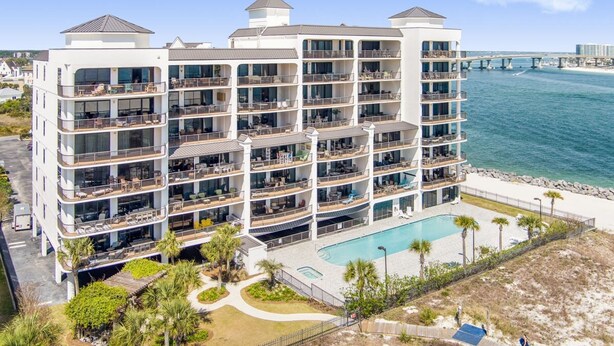 A multi-story hotel with balconies, a swimming pool, and a view of the ocean and a bridge in the background. - Grand Pointe 502- Gulf-front Water on 2 Sides (Orange Beach)