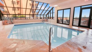 An indoor swimming pool with clear glass walls, a metal ladder, and a view of a building with balconies. - Four Seasons 502-e Pier Newly Remodeled (Orange Beach)