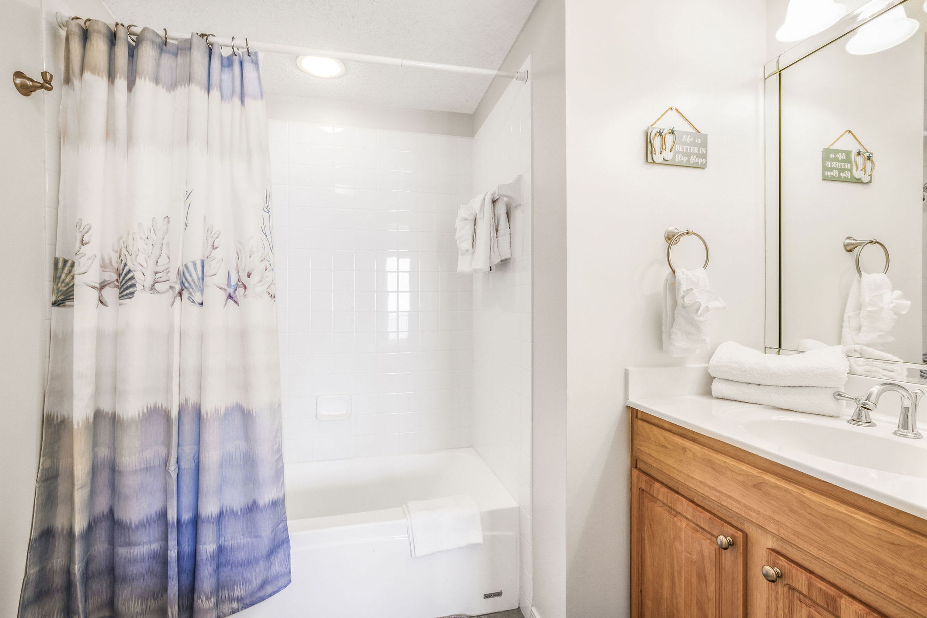 A bathroom with a shower curtain, a bathtub, a vanity with a mirror, and towels.