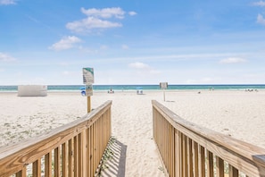 A wooden boardwalk leading to a beach with clear skies and calm waters.