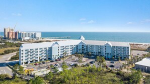 A large hotel with multiple floors and a parking lot, located near a beach and ocean. - Grand Caribbean Pool Gym Beach View (Orange Beach)