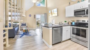 A modern kitchen with a central island, stainless steel appliances, and a dining area with a blue rug. - Grand Caribbean Pool Gym Beach View (Orange Beach)