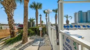 A beachfront view with palm trees, a no dogs allowed sign, and a row of blue beach chairs. - Grand Caribbean Pool Gym Beach View (Orange Beach)