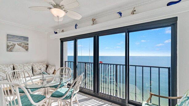 En balkon med udsigt over havet, hvide fletmøbler og en loftsvifte.