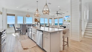 A modern kitchen with a large island, pendant lighting, and a view of the ocean. - Lil Tip Sea 8 BR Private Pool Elevator Beach (Gulf Shores)