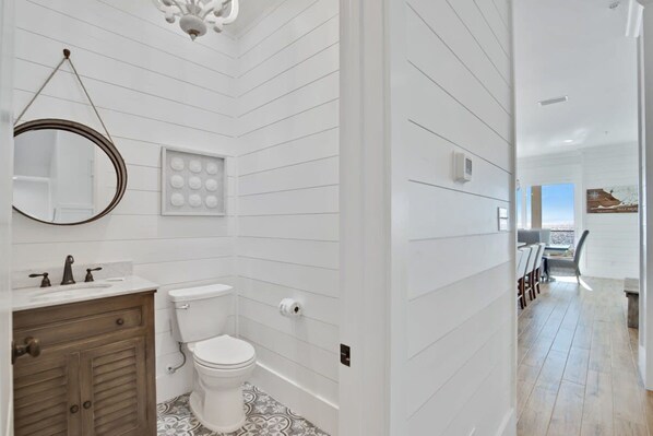 A modern bathroom with a white tiled wall, a wooden vanity, a toilet, and a patterned floor. - Lil Tip Sea 8 BR Private Pool Elevator Beach (Gulf Shores)