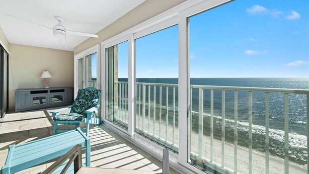 Een balkon met uitzicht op de oceaan, een plafondventilator en een zithoek met een stoel en een tafel.