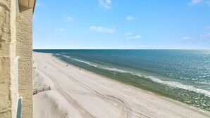 Uitzicht op het strand vanaf een balkon, met heldere lucht en een rustige zee.