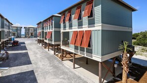 Eine Reihe von Strandhäusern mit erhöhten Plattformen und roten Fensterläden, verbunden durch einen überdachten Gang.