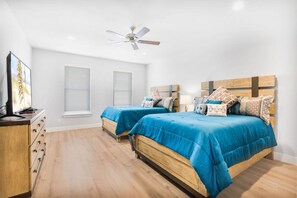 Two beds with blue bedspreads and patterned pillows, a dresser, and a ceiling fan.
