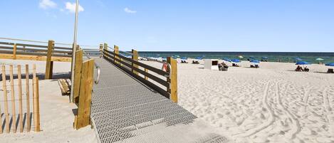 A wooden boardwalk leading to a beach with a flagpole displaying the American flag and a yellow flag.