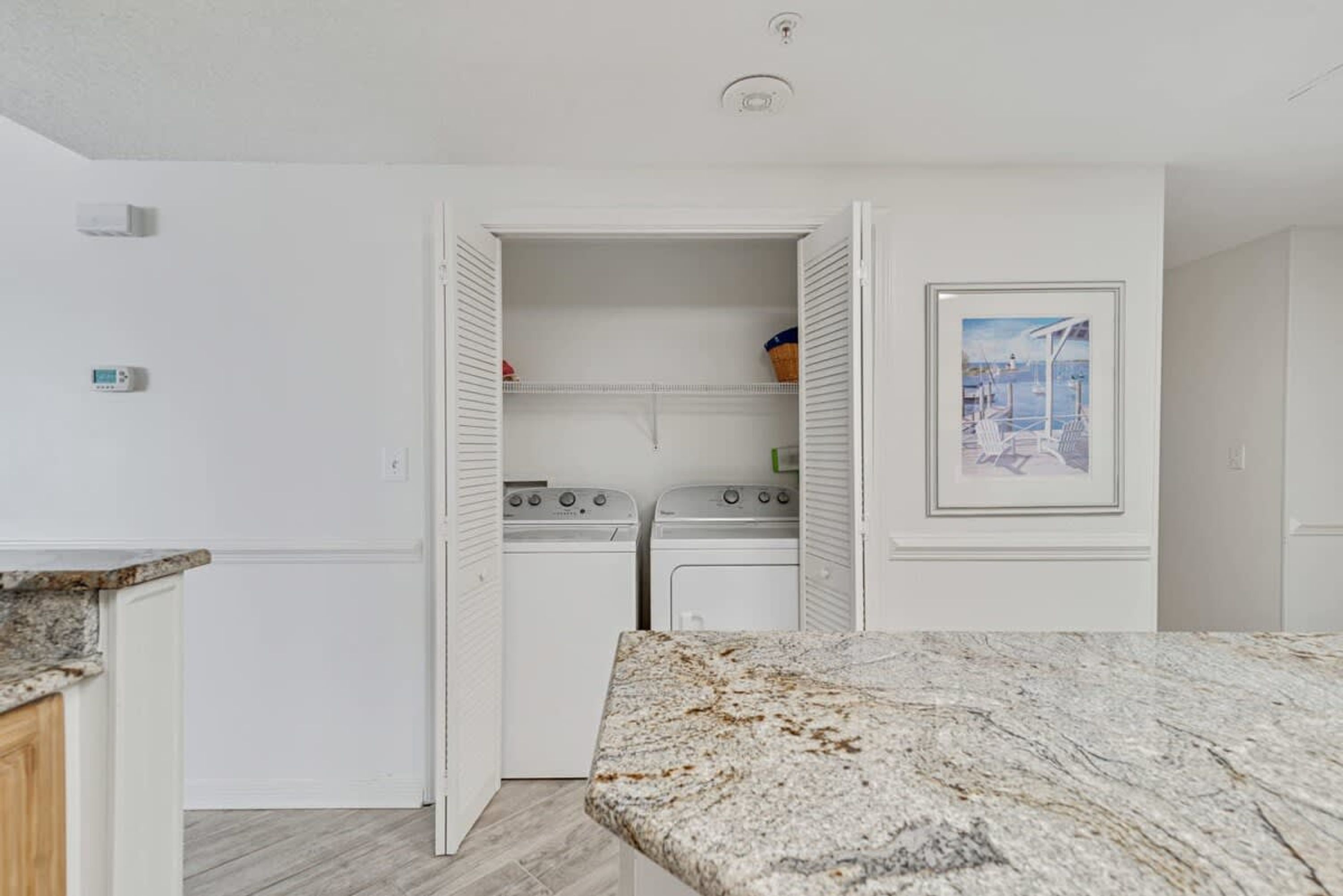 A laundry room with a white interior, a granite countertop, and a framed picture on the wall.