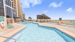 Una piscina con lettini e una zona relax coperta, circondata da un grattacielo.
