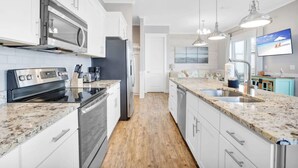 Eine moderne Küche mit weißen Schränken, Granit Arbeitsplatten und Edelstahlgeräten, beleuchtet durch Pendelleuchten.