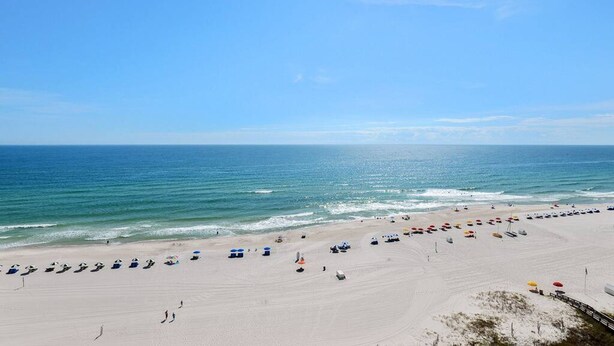 A wide beach with rows of umbrellas and beach chairs, a clear sky, and the ocean in the background. - Pelican Pointe1204 3BR 2BA Gulf-front (Orange Beach)