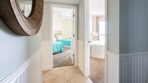 A hallway leading to a bedroom with a bed, a nightstand, and a lamp. - Pelican Pointe1204 3BR 2BA Gulf-front (Orange Beach)