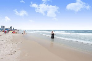 A beach with a clear sky, people walking along the shore, and umbrellas set up on the sand.