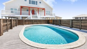 Un espace piscine avec une terrasse en bois, un bâtiment blanc doté d’une porte rouge et un panneau sur lequel on peut lire : « Cher Temps ».