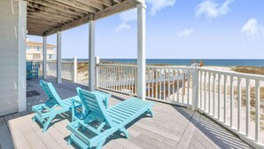 Un espace extérieur abrité doté d’une terrasse en bois, de rampes blanches et de deux chaises longues turquoise.