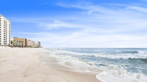 Ein Strand mit sandigem Ufer und Wellen. Entlang des Strandes befinden sich Gebäude.