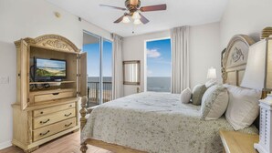 A bedroom with a large bed, a television on a wooden cabinet, a ceiling fan, and a view of the ocean through a sliding door. - Spanish Key 504 Next to Flora-bama Sleeps 9 (Pensacola)