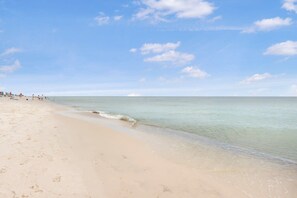 A wide sandy beach with gentle waves, a clear sky, and a few people in the distance. - Spanish Key 504 Next to Flora-bama Sleeps 9 (Pensacola)