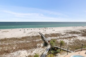 A beach resort with a wooden boardwalk leading to a pool area, surrounded by sand dunes and sparse vegetation. - Spanish Key 504 Next to Flora-bama Sleeps 9 (Pensacola)