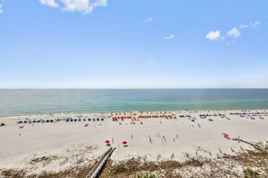 A beach with numerous umbrellas and beach chairs, a wooden walkway, and a clear view of the ocean.
