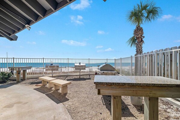 Un área de patio al aire libre con mesas y bancos de hormigón, una valla de madera y vistas a la playa y al océano.