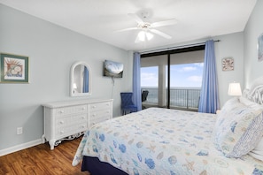 A bedroom with a large bed, a dresser, a ceiling fan, and a view of the ocean through a sliding door. - Windward Pointe 801 East Corner-unit Beachfront (Orange Beach)