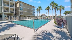 A swimming pool with a white fence, palm trees, and a building with balconies. - Portside 204 Best of Beach Bay (Pensacola)