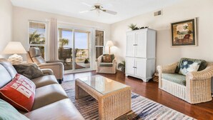 A spacious living room with a glass coffee table, leather sofas, wicker armchairs, and a white cabinet. - Portside 204 Best of Beach Bay (Pensacola)