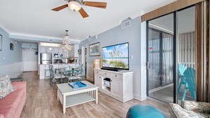 A spacious living area with a ceiling fan, a dining table with chairs, a television, and a sliding glass door leading to an outdoor area.