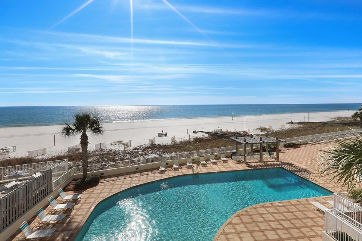 A poolside view with a beach and ocean in the background.