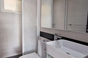 A modern bathroom with a white sink, a mirror, and a shower area.