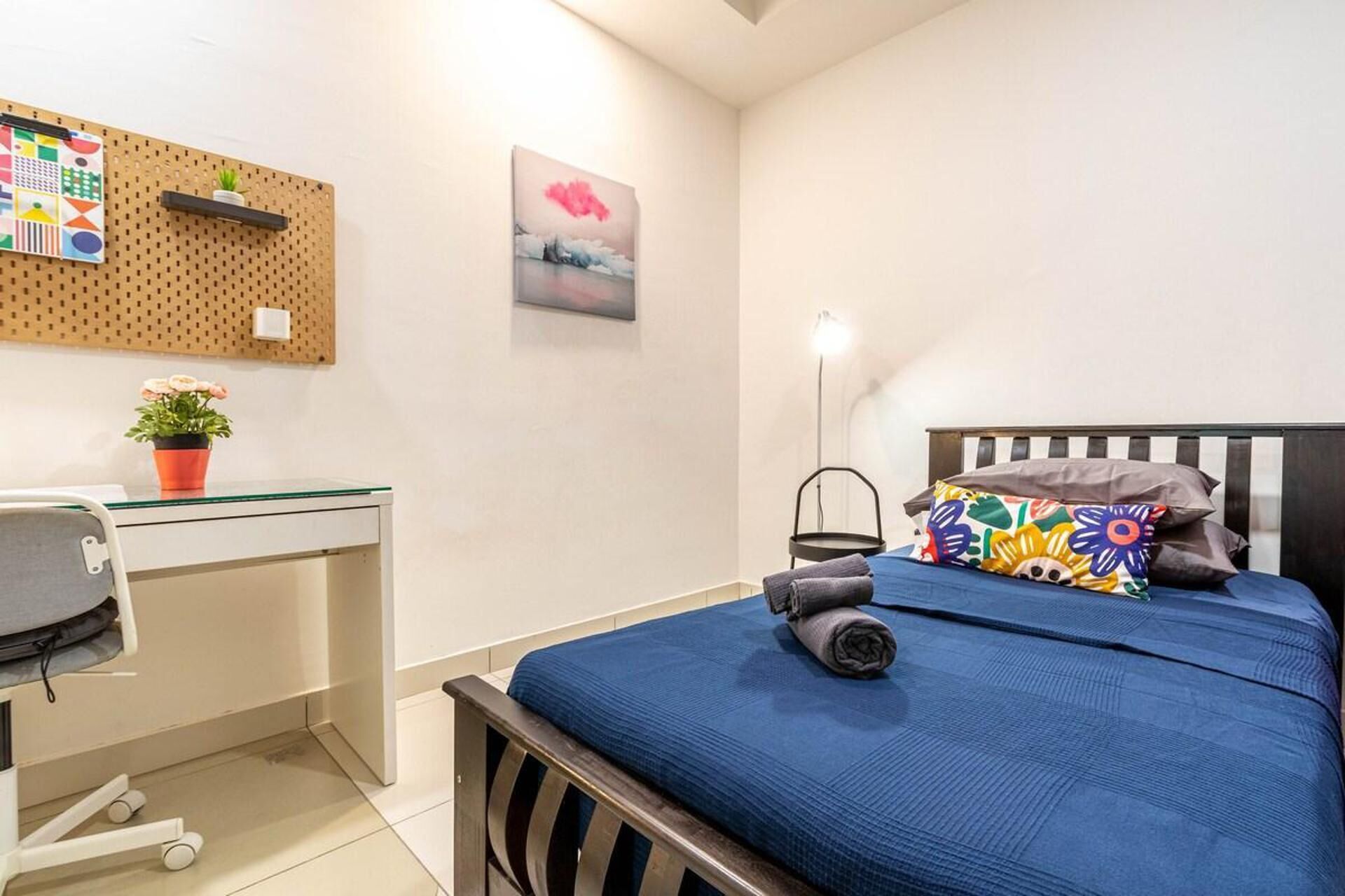 A bedroom with a bed, a desk, a chair, a wall-mounted pegboard, and a painting.