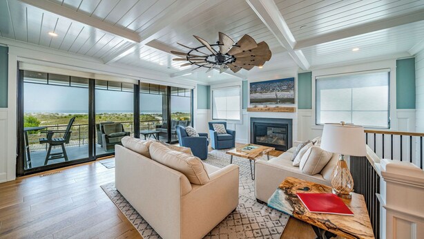 A spacious living area with a large sofa, a fireplace, and a view of the beach.