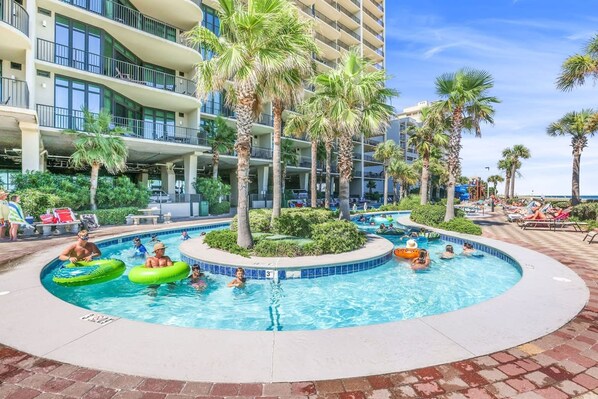 A pool area with multiple levels of balconies, palm trees, and a clear blue sky.