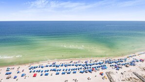 Ein Strand mit Reihen blauer Sonnenschirme und Liegen, einem klaren Himmel und dem Meer.