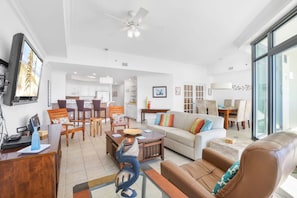 A spacious living room with a sofa, coffee table, and chairs, a dining area with a table and chairs, and a kitchen in the background. - Phoenix West 2508 Views Galore 3 4 Lazy River (Orange Beach)