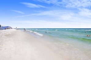 A beach with clear skies, calm waters, and people swimming.
