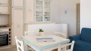 A compact kitchen with a dining area, featuring a table with chairs, a small potted plant, and a blue sofa. - Villa Azzurra by Propertize - a few steps from the sea (Pittulongu)